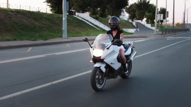 En kvinna åker motorcykel i början av solnedgången - höjer glaset på skyddshjälmen — Stockvideo