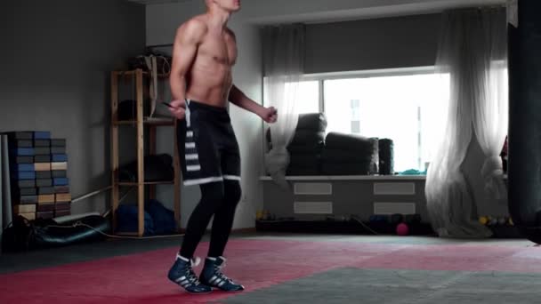 Молодий чоловік у тренажерному залі тренує свою витривалість - стрибає через мотузку — стокове відео