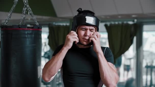 Ung man boxare sätter på sig en skyddande boxningshjälm och står i skyddande ställning — Stockvideo