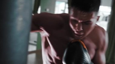 Gömleksiz genç adam kum torbasını yumrukluyor.