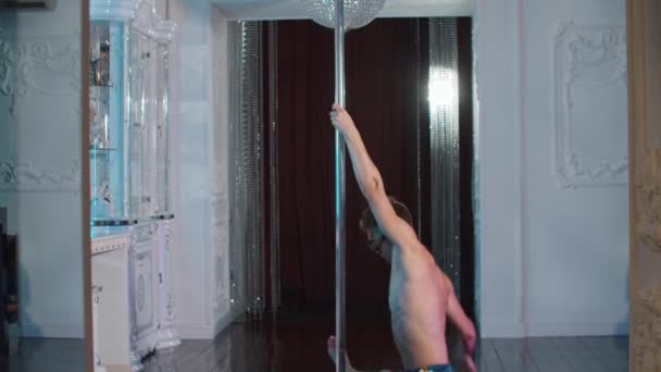 Een jonge shirtloze man expressief dansen aan de paal in glazen met strass steentjes in de studio — Stockvideo