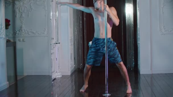 Een jonge zelfverzekerde shirtloze man expressief dansen aan de paal in glazen met strass steentjes in de studio — Stockvideo