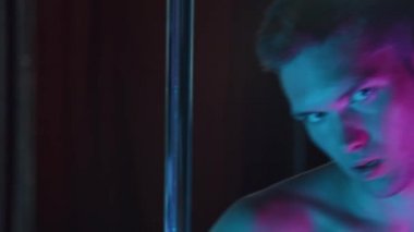 Genç çapkın bir striptizci neon ışıkta seksi davranıyor ve şarkı söylüyor.