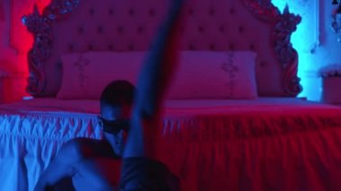 Genç striptizci seksi davranıyor ve neon ışıklı zeminde dans ediyor yatağa oturuyor ve dansına devam ediyor.