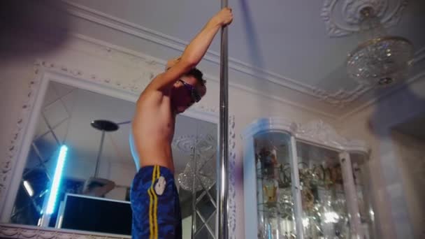 Ung shirtless mand stripper i nuancer dækket med rhinestones og iført strand shorts bizar dans ved stangen – Stock-video