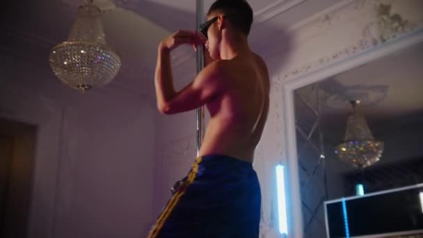 Joven stripper hombre sin camisa en tonos cubiertos de pedrería extraña danza por el poste en el estudio — Vídeo de stock