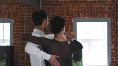 Erkek ve kadın kostümlü olarak stüdyoda tuğla duvarlarla dans ediyorlar.