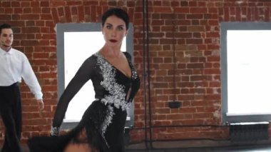 Kostüm giyen bir çift, dans numaralarını turuncu duvarlı stüdyoda eğitiyorlar.