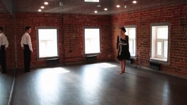Atrakcyjna para ćwicząca taniec - kobieta rozpoczyna taniec, a jej mężczyzna obserwuje ją z kąta pokoju — Wideo stockowe