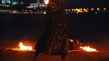 Sahilde ateşle oynayan parlak elbiseli bir adam ve kadın.