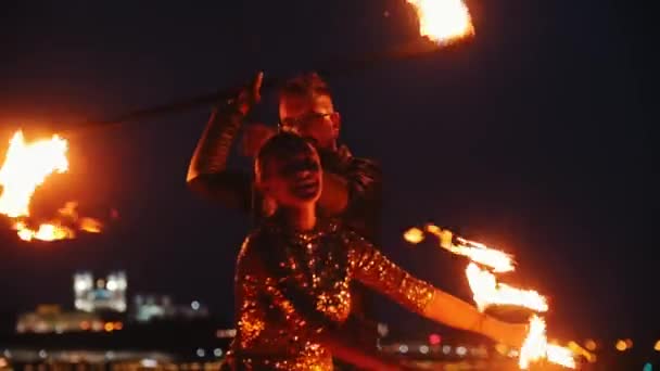 Fire show performance - άνδρας και γυναίκα με λαμπερά ρούχα που παίζουν με τη φωτιά στη νυχτερινή παραλία — Αρχείο Βίντεο