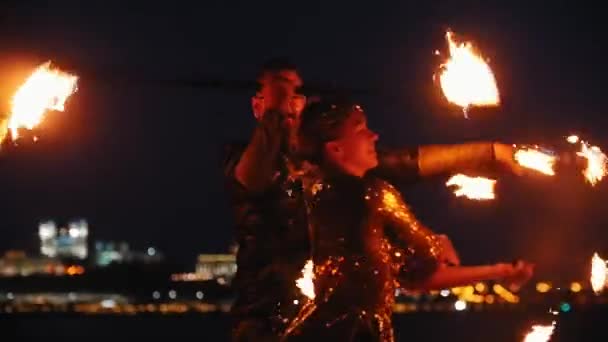 Desempenho de show de fogo homem e mulher em uma roupa brilhante dançando com tochas de fogo na praia noturna — Vídeo de Stock
