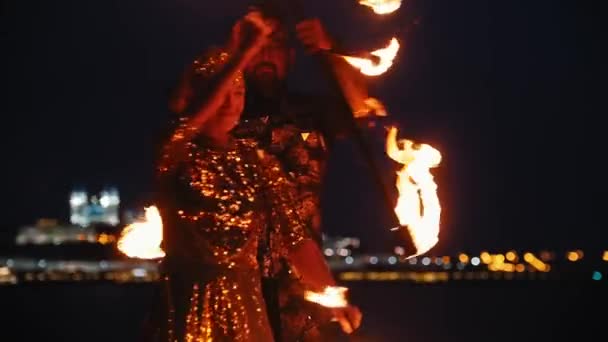 Tűzvész show - nő és férfi fényes ruhákban teljesítő tűz fáklyák az éjszakai strandon — Stock videók