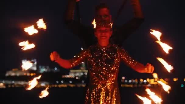 Show de fogo - mulher em um vestido brilhante e homem atrás dela realizando com tochas de fogo na praia noturna — Vídeo de Stock