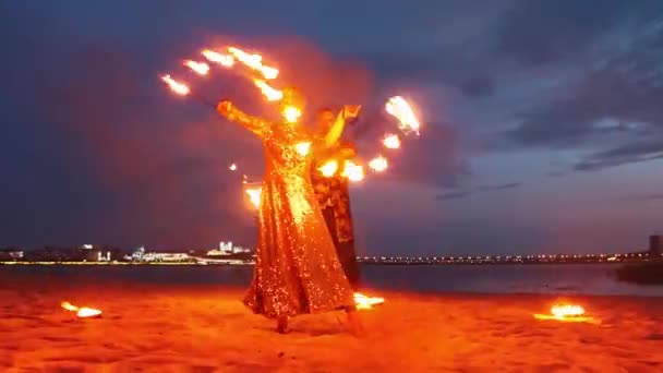 Огненное шоу - мужчина и женщина танцуют с факелами на пляже поздно вечером — стоковое видео