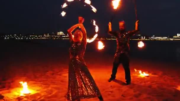 Show de fogo mulher e homem dançando com tochas na praia na cidade no final da noite — Vídeo de Stock