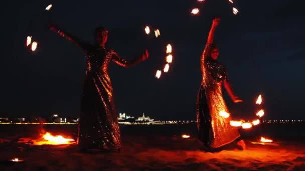 Огненное шоу - две женщины в блестящих платьях танцуют синхронно с зажженными факелами — стоковое видео