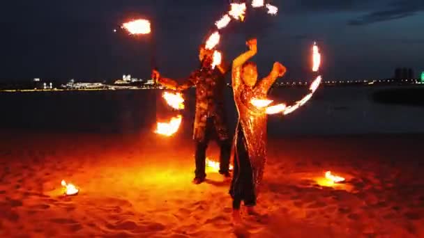 Show de fogo - mulher sorridente em vestido brilhante e um homem de traje dançando com tochas acesas na praia — Vídeo de Stock