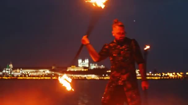 Fire show performance - muž v lesklém kostýmu tančící se dvěma pochodněmi na noční pláži — Stock video