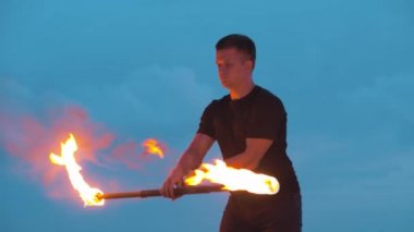 Siyah elbiseli genç adam gecenin geç saatlerinde çift taraflı ateş meşalesiyle oynuyor.