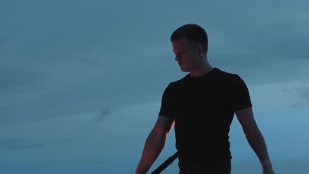 Mladý muž performer v černém oblečení tančí s ohněm pochodeň v rukou na pozadí tmavě modré oblohy — Stock video
