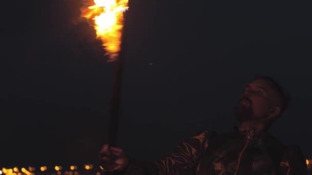 髭を生やした男が夜のビーチの火の上でガソリンを吐き出す — ストック動画