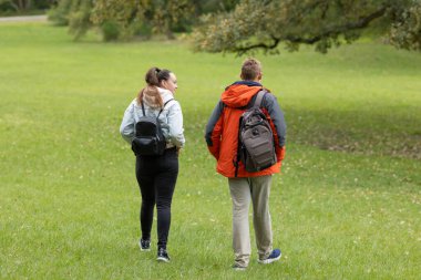 Sırt çantalı iki genç, yemyeşil bir çimenlikte yürüyorlar.