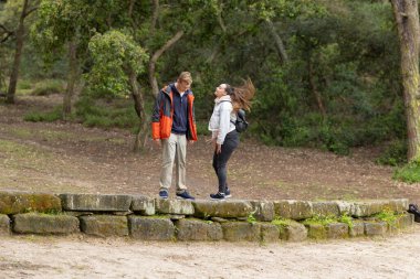 Genç bir adam ve bir kadın gülüyor, bir ormanda taş bir duvarda neşeyle etkileşime geçiyorlar.