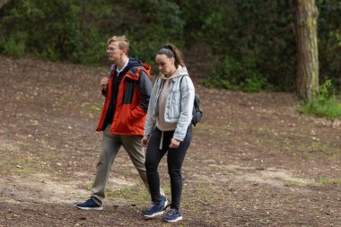 Genç bir adam ve kadın ağaçlık bir parkta kirli bir yolda yürüyorlar.