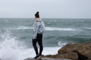Genç bir kadın fırtınalı bir günde büyük dalgaların düşüşünü seyrediyor.
