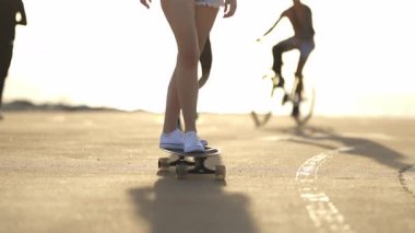 Güneşli bir günde uzun bir sörf tahtasına binen genç kadınlar durup tahtayı alırlar.