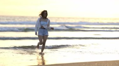 Güzel bir altın saat gün batımında sahilde koşan ve gülümseyen neşeli kadın.