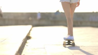 Güneşli bir günde beton bir parkta kaykay yapan genç bir kadının arka görüntüsü.