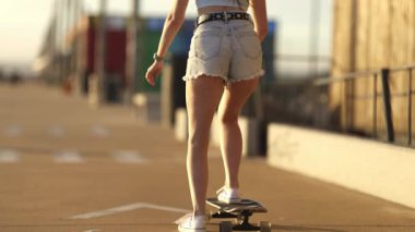 Güzel, güneşli bir yaz gününde tahta kaldırımda kaykay yapan genç bir kadın.