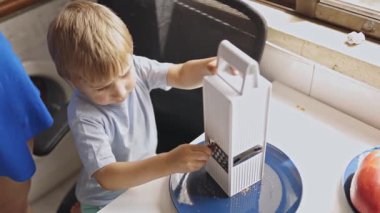 Dikkatle odaklanmış genç bir çocuk parlak bir mutfakta bir parça çikolatayı mavi bir tabağa ızgara yapıyor.