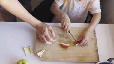 Bir anne ve oğulun ellerinin masada tahta bir tahtanın üzerinde taze bir elma kesişinin en üst görüntüsü.