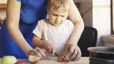 Şefkatli bir anne, küçük oğluna evdeki tahtadan taze elma kesmeyi öğretiyor.