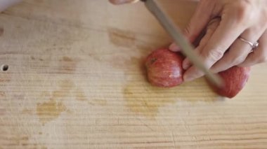 Anneler, çocuğuna tahta bir tahtanın üzerinde kırmızı bir elmayı dikkatlice kesmesi için rehberlik eder.