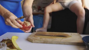 Kadın elleri tahta bir tahtada olgun bir nektarin keserken bir çocuk arka planda bekliyor.