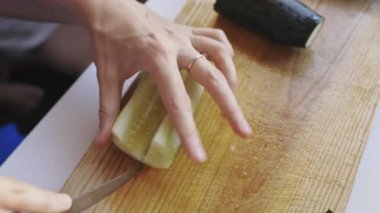 Mutfaktaki ahşap bir tahtanın üzerinde taze yeşil bir salatalık kesen kadın ellerini kapatın.