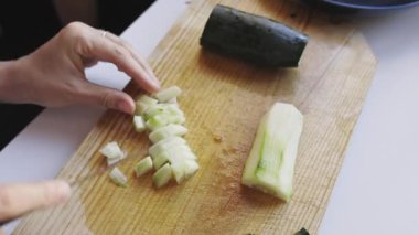 Taze salata için tahta bir tahtanın üzerinde bir bıçakla salatalığı kesen kadın ellerini kapatın.