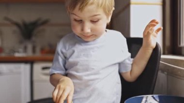 Küçük çocuk mutfaktaki tahta bir tahtada bıçakla taze sarı bir mangoyu dikkatlice kesiyor.