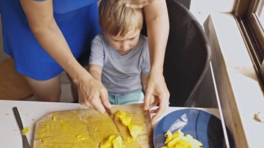 Küçük oğlu için kesme tahtasında taze sarı meyve doğrayan bir annenin tepeden aşağı bakışı.