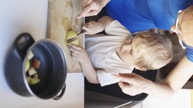 Anne ve oğlu mutfakta birlikte yemek pişiriyor, kesme tahtasında elma kesiyorlar.