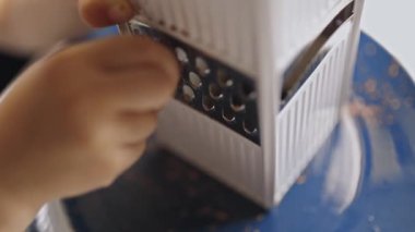 Küçük çocuklar mavi tabakta metal rendeleyicisi olan lezzetli siyah çikolata rendeliyorlar.