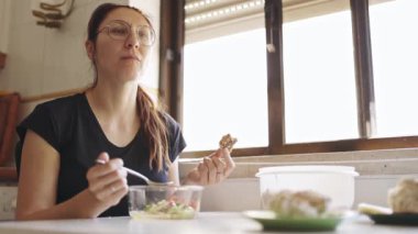 Kızıl saçlı kadın taze sebze salatasının ve pencerenin yanında bir parça ekmeğin tadını çıkarıyor.