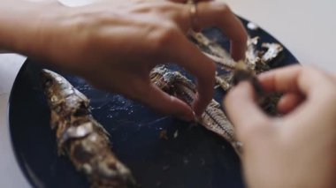 İnsan elleri yemeden önce küçük kızarmış balıkları koyu mavi bir tabakta temizler ve kemiklerinden ayırır.