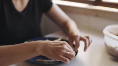 İsimsiz bir kadın elleriyle ızgara balık yiyor. Mavi bir tabakta eti kemiklerden ayırıyor.