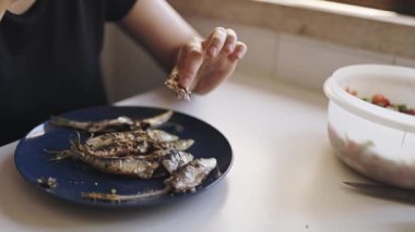 Kadınların elleri, mutfakta mavi bir tabakta ızgara sardalyadaki kemikleri ustalıkla temizler.
