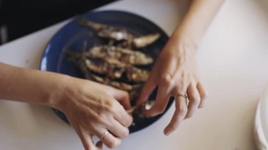 Kadınsı eller, yemeden önce mavi bir tabakta taze ızgara sardalya temizler.